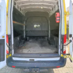 Wnętrze puste, brudne, białego busa z żółtymi elementami, widok z tyłu na otwarte drzwi, na ścianie gaśnica.