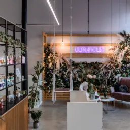 Nowoczesne wnętrze salonu kosmetycznego z huśtawką, neonem 'Ultrafiolet' i regałem z kosmetykami, dekoracje z roślin i kwiatów.