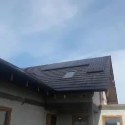 Montaż paneli słonecznych na dachu domu w trakcie budowy, widok na dachówkę i okno dachowe.