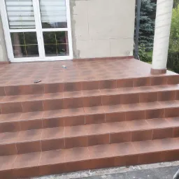 Wykończone płytkami schody wejściowe do domu z kolumną dekoracyjną, widoczne narzędzia i resztki zaprawy.