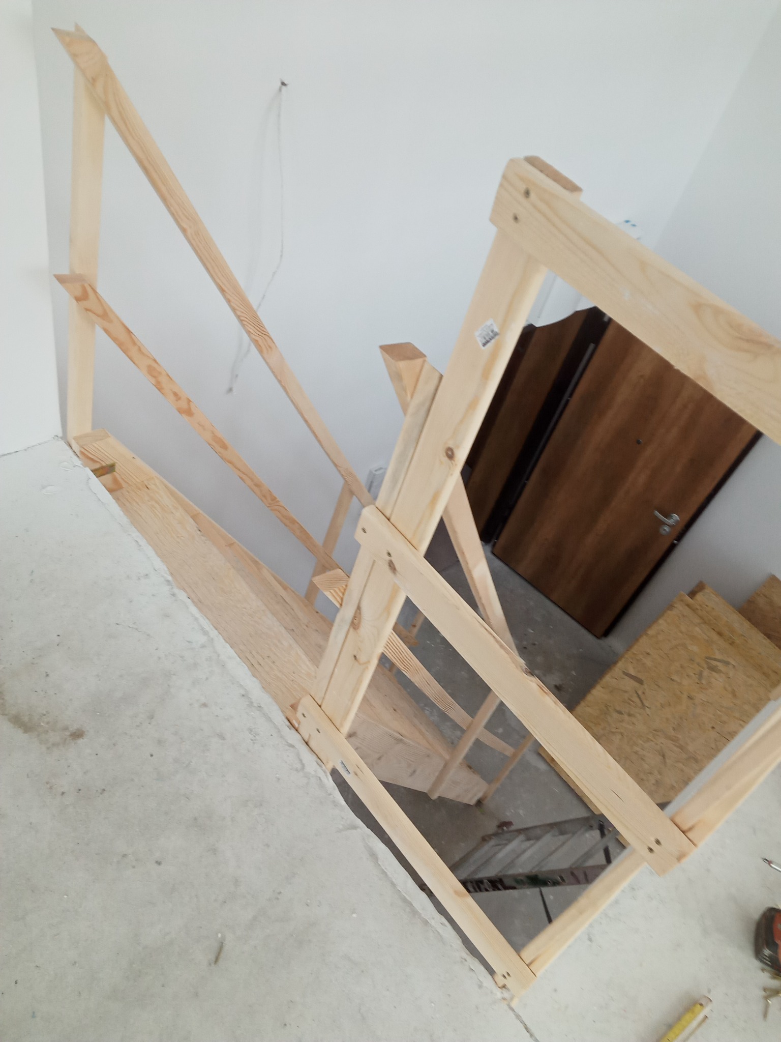 Konstrukcja drewnianych schodów w surowym stanie, widok z góry, w tle drzwi i płyty OSB.