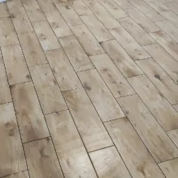 Ułożona podłoga z płytek imitujących drewno, widoczna butelka z napojem przy ścianie z odsłoniętą cegłą.