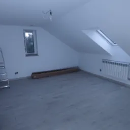 Poddasze po remoncie: białe ściany, jasna podłoga z paneli, okno dachowe, grzejnik, drabina, profile do płyt karton gips na ścianie, przygotowane panele w kartonie.