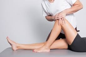 Fizjoterapeuta uciska kolano pacjentki leżącej na stole do masażu, skupienie na technice manualnej.