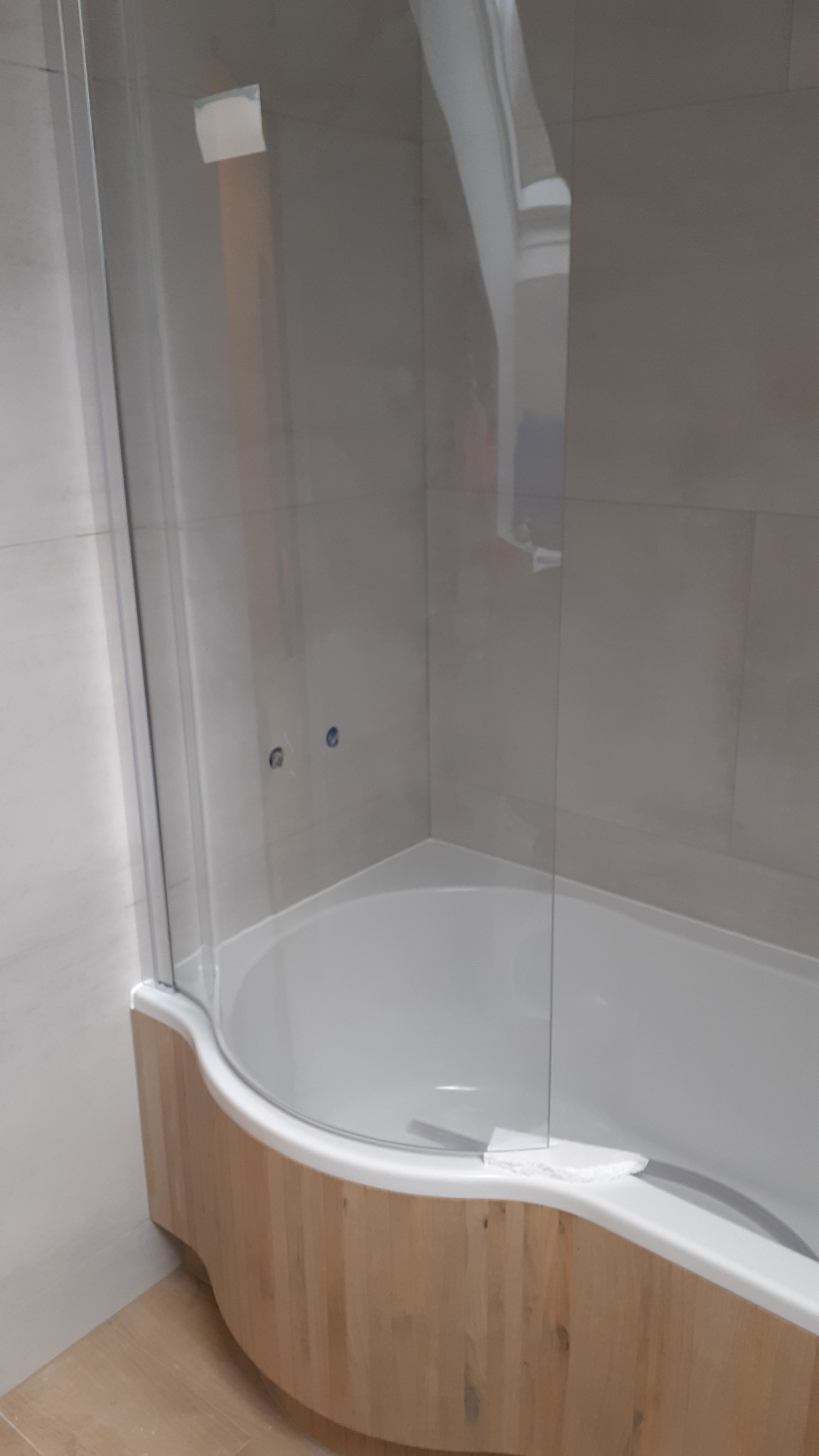 Szklana kabina nawannowa z drewnopodobną obudową, widoczne płytki w jasnych odcieniach i fragment podłogi.