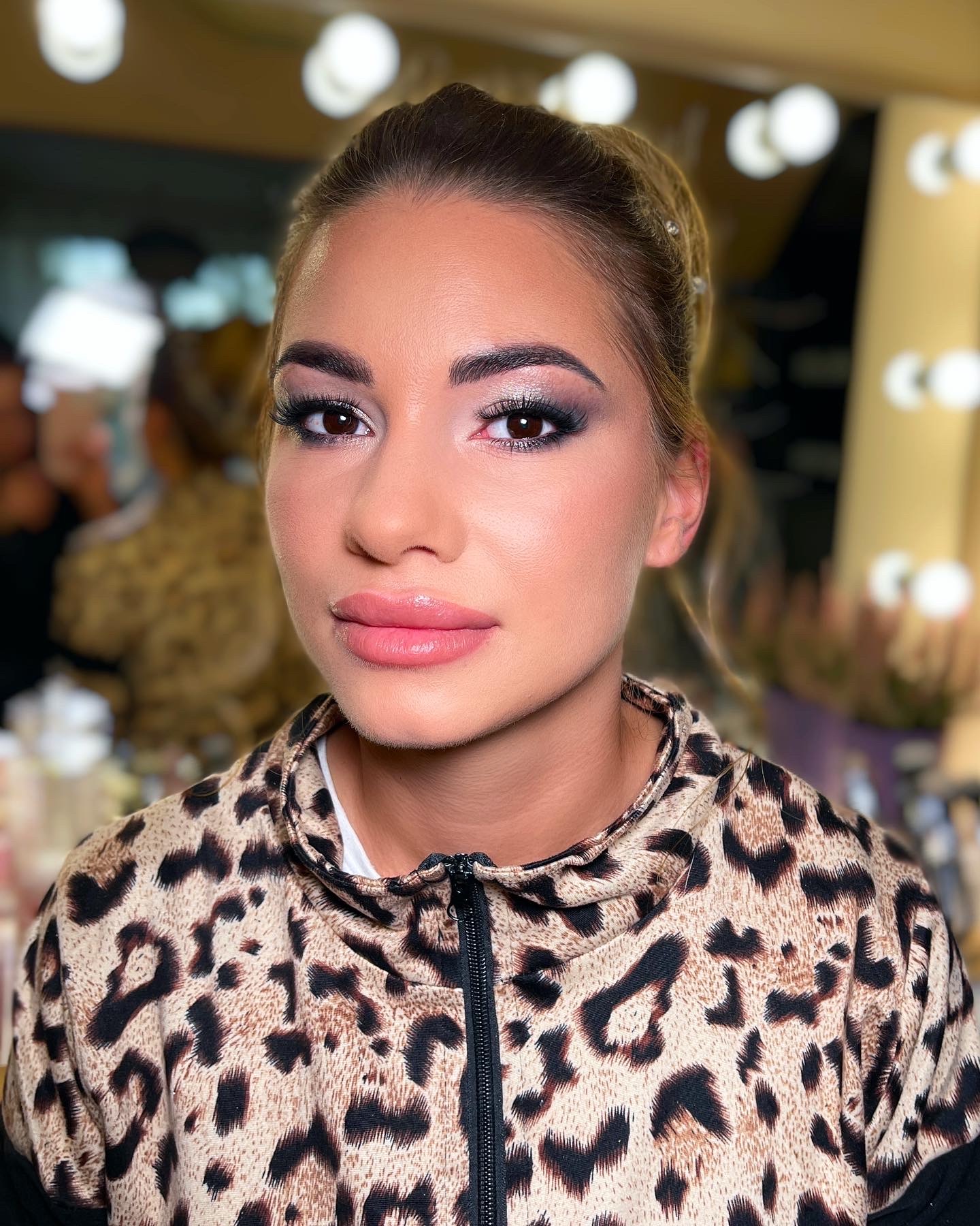 Portret kobiety z profesjonalnym, wieczorowym makijażem w Katowicach, z uwydatnionymi oczami i delikatnymi ustami na tle lustra z oświetleniem.