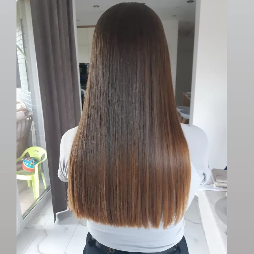 Długie, proste włosy w odcieniach brązu, z ciemniejszymi odrostami i jaśniejszymi końcówkami, widoczne od tyłu, z delikatnym połyskiem.