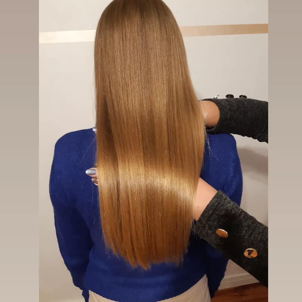 Proste, lśniące, miodowe włosy sięgające do pasa, prezentowane z tyłu, dłonie w szarych rękawach z guzikami delikatnie je podtrzymują.