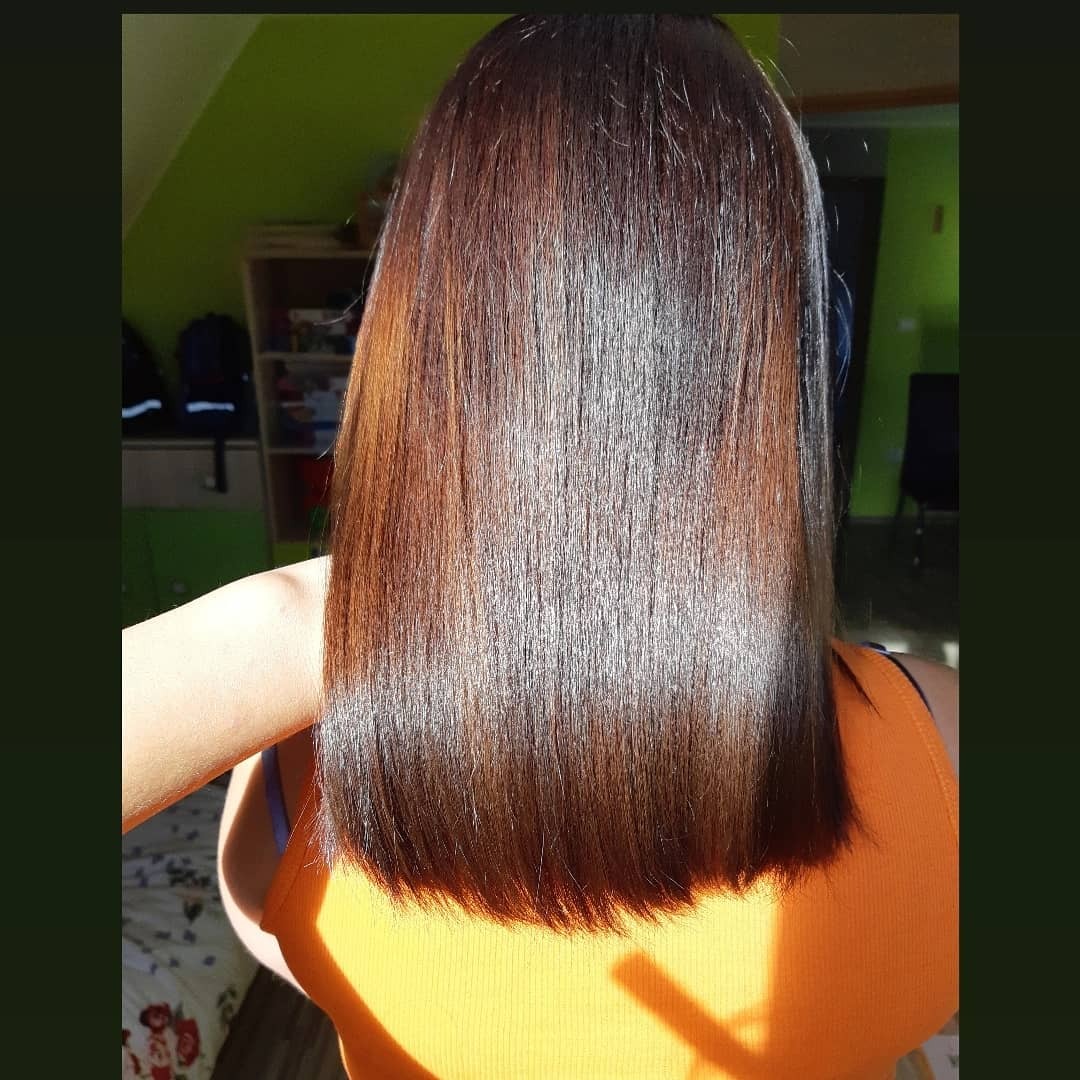 Proste, lśniące, ciemnobrązowe włosy, widok z tyłu, z delikatnym cieniowaniem końcówek, oświetlone naturalnym światłem słonecznym.