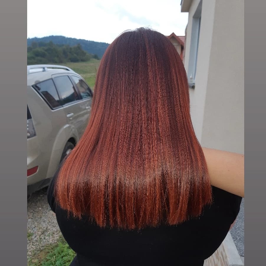 Długie, proste włosy w odcieniach miedzi i brązu, widoczne od tyłu, na tle domu i górskiego krajobrazu.