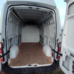 MATCARS POMOC DROGOWA Wynajem busów GIŻYCKO - Wnętrze białego, pustego furgonu z otwartymi tylnymi drzwiami, ukazujące przestrzeń ładunkową z drewnianą podłogą i widocznymi elementami konstrukcyjnymi.