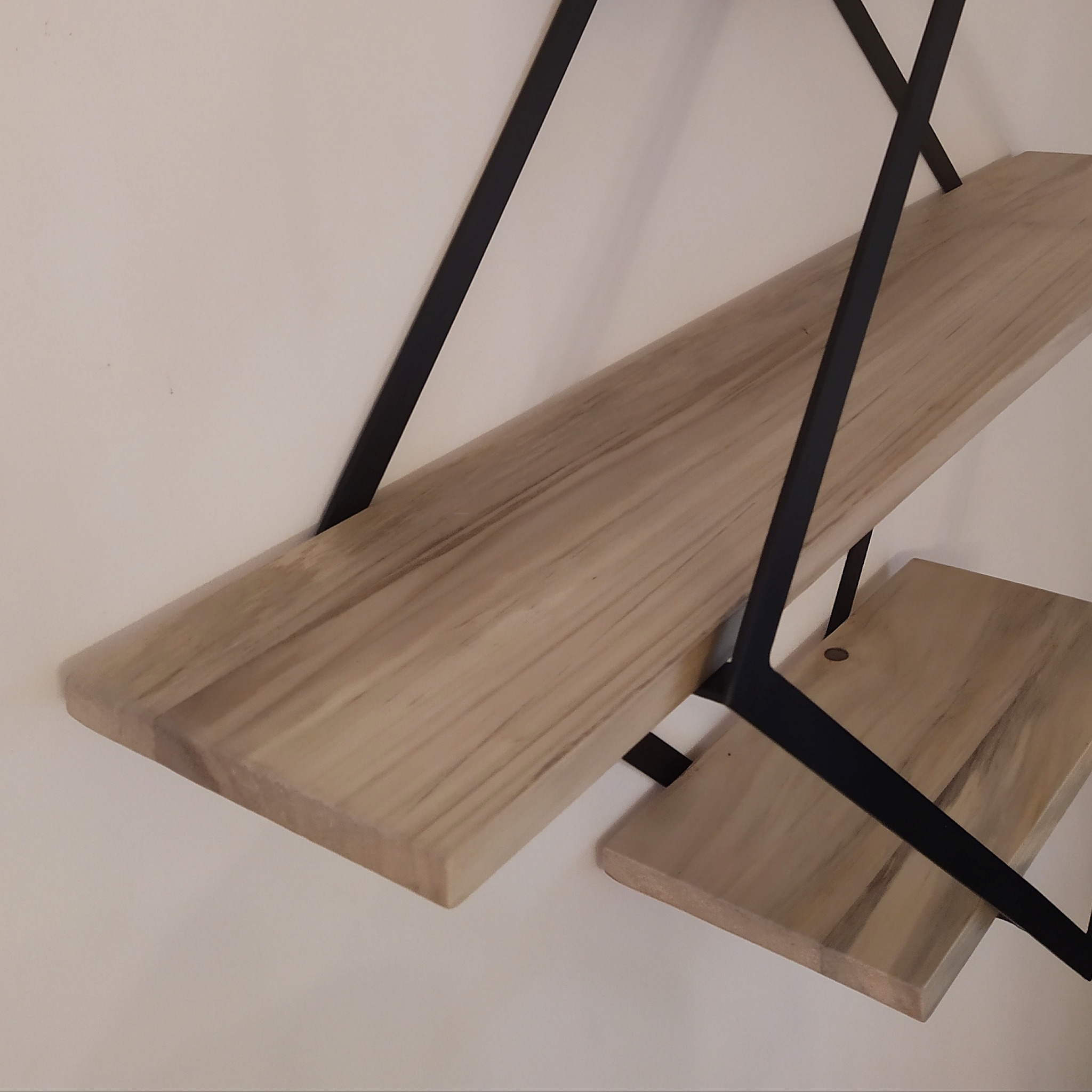 Dwie półki z jasnego drewna zamocowane na ścianie za pomocą czarnych, metalowych wsporników w kształcie litery X.