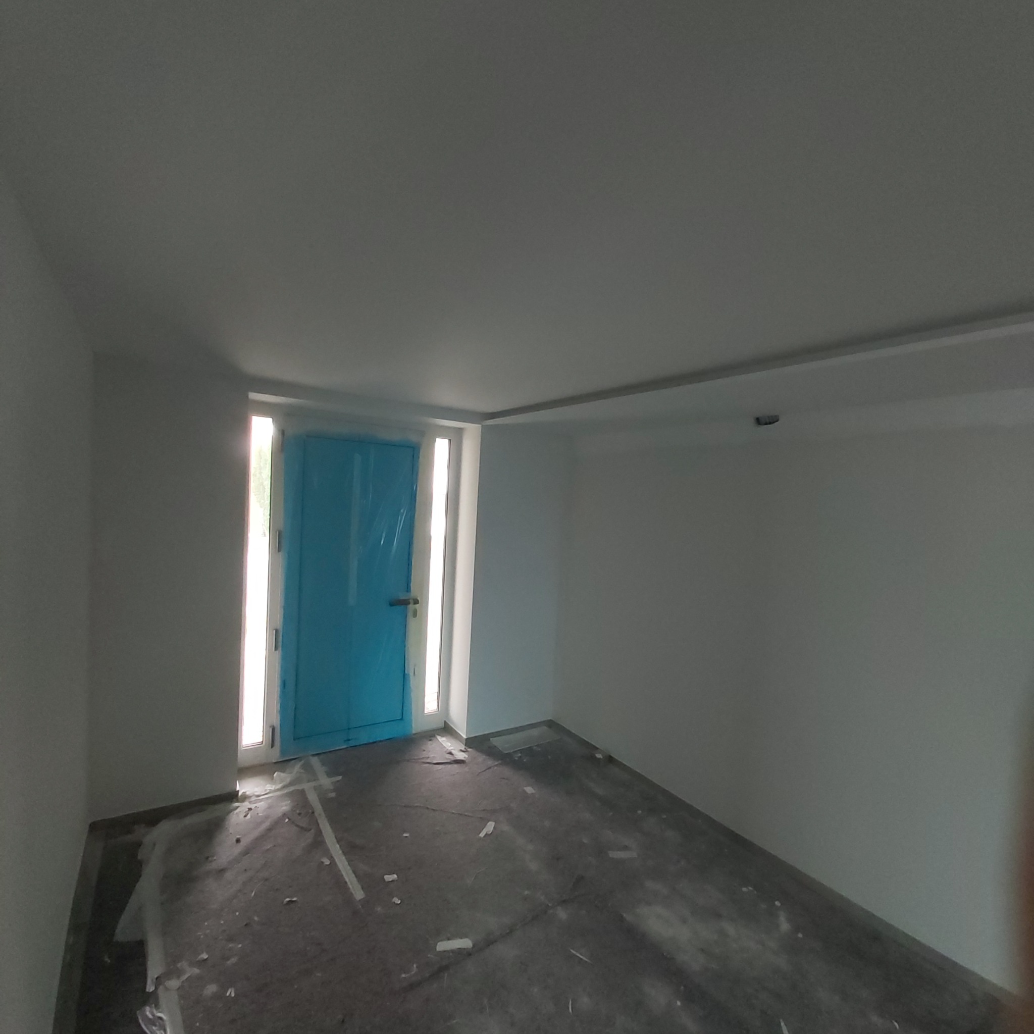 Łazienka w trakcie malowania: drzwi zabezpieczone folią, podłoga przykryta folią ochronną, świeżo pomalowane ściany na biało.