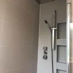 Nowoczesna kabina prysznicowa z deszczownicą i słuchawką, wykończona beżowymi płytkami, z wnęką na kosmetyki i minimalistyczną armaturą.