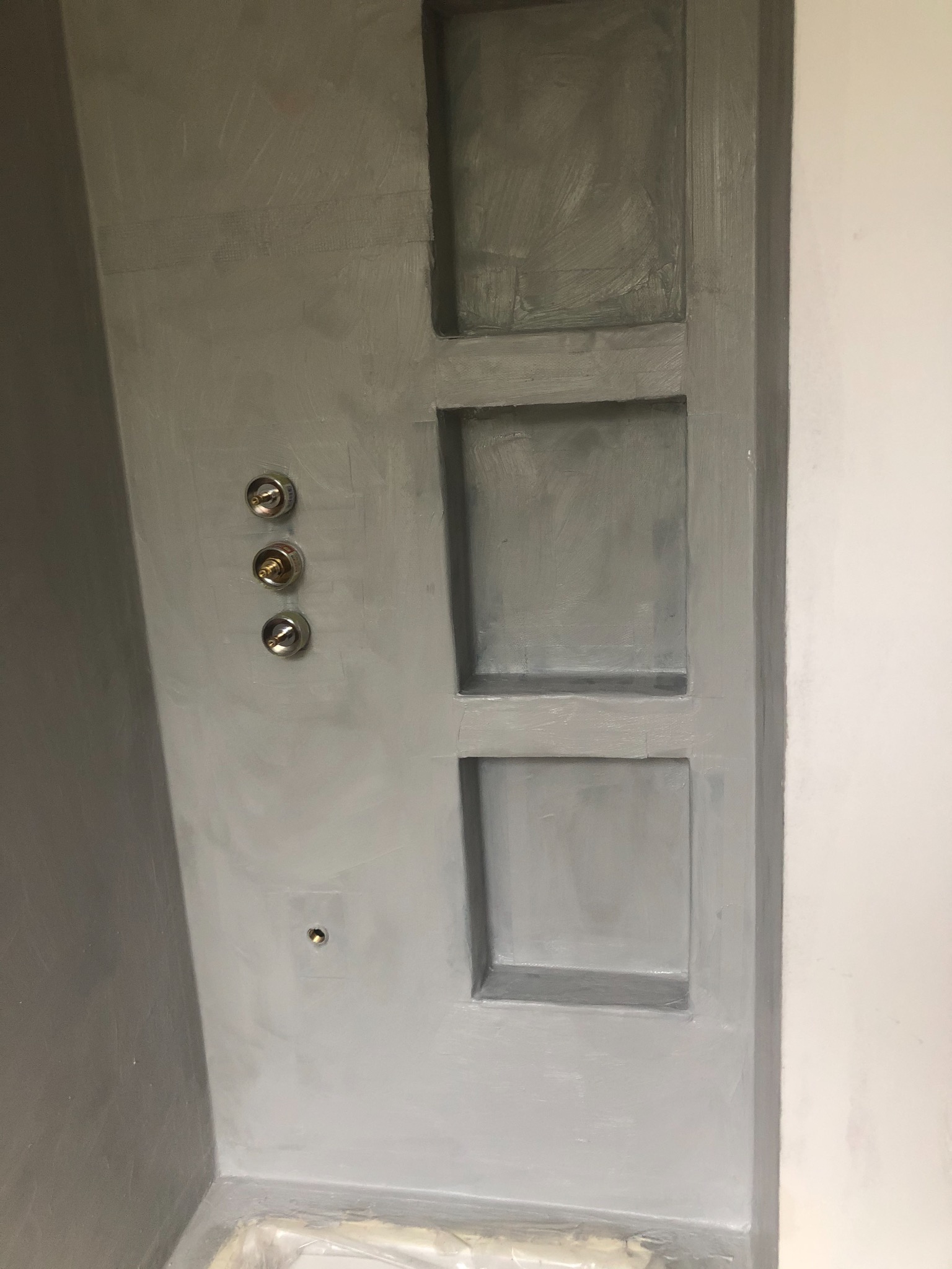 Szara ściana w łazience z trzema metalowymi zaworami i wnękami w kształcie kwadratów, świeżo po malowaniu.