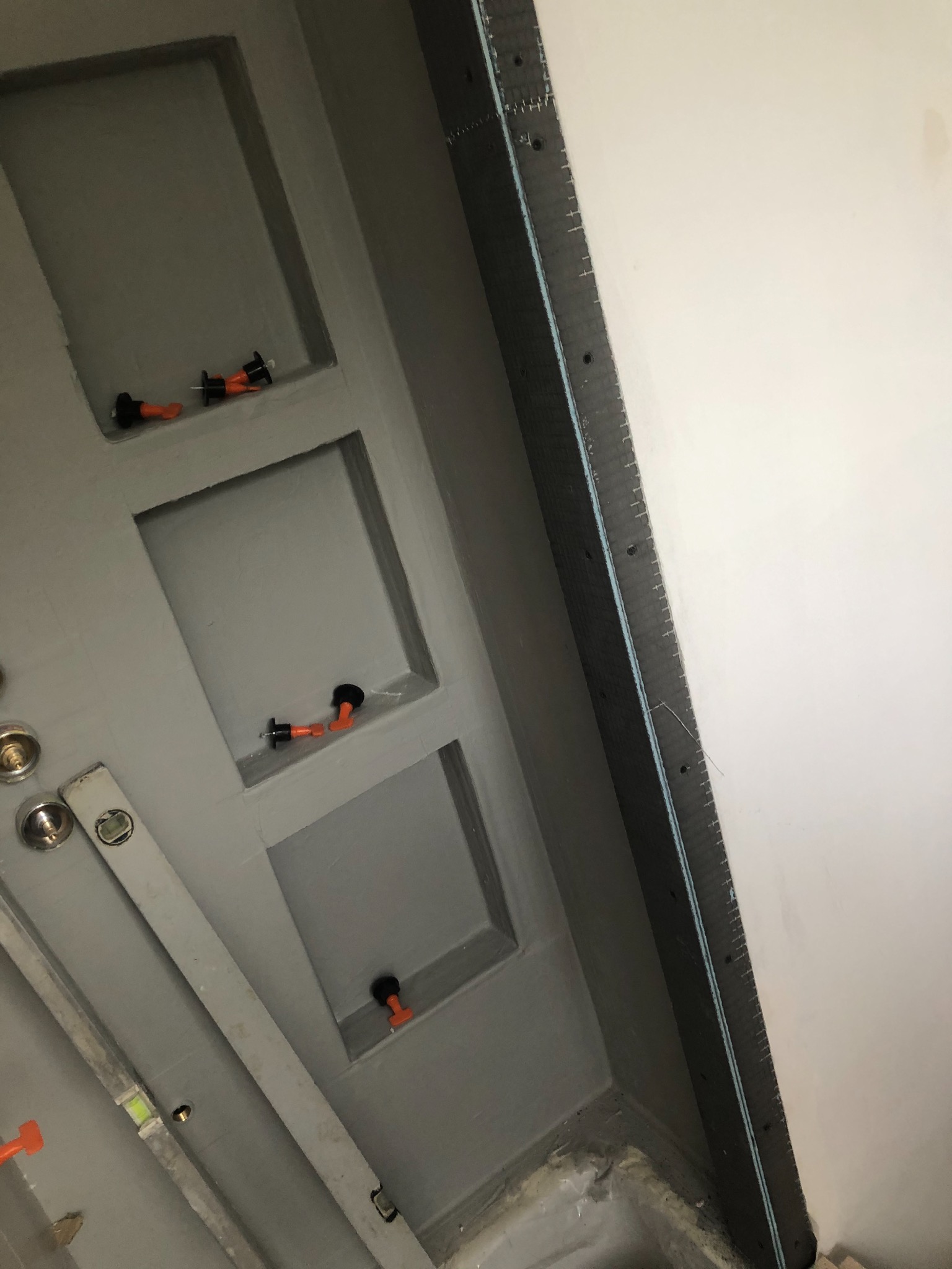 Ściana z wnękami w trakcie szpachlowania, widoczne poziomice i klipsy do płytek, przygotowanie do wykończenia.