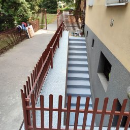 karmarRemonty Marcin Pański - Świeżo pomalowane szare schody zewnętrzne prowadzące do budynku z żółto-szarą elewacją, widoczne puszki z farbą, brązowe ogrodzenie po lewej stronie.