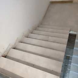 karmarRemonty Marcin Pański - Klatka schodowa w trakcie wykańczania: widoczne surowe ściany, białe stopnie schodów oraz fragment podłogi z ułożonymi płytkami.