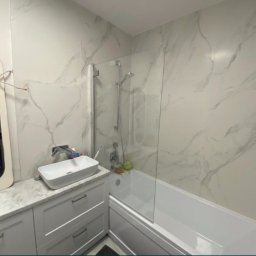 karmarRemonty Marcin Pański - Nowoczesna łazienka z wanną za szklanym parawanem, umywalką nablatową i dużymi płytkami imitującymi marmur na ścianach, odbicie osoby robiącej zdjęcie w lustrze.