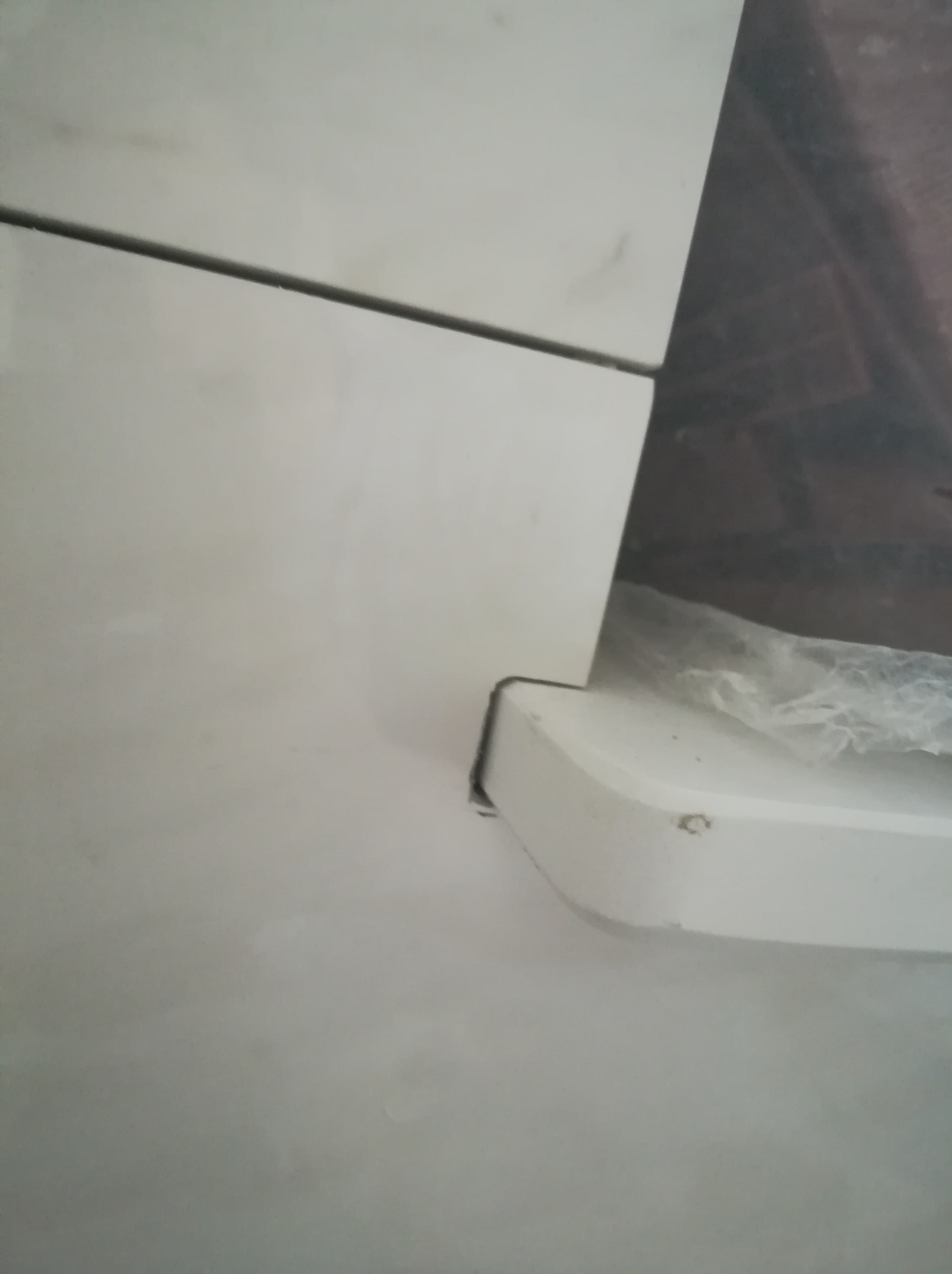 Fragment białej zabudowy, prawdopodobnie meblowej, z widocznymi łączeniami i drobnymi niedoskonałościami wykończenia, sfotografowany z bliskiej odległości.