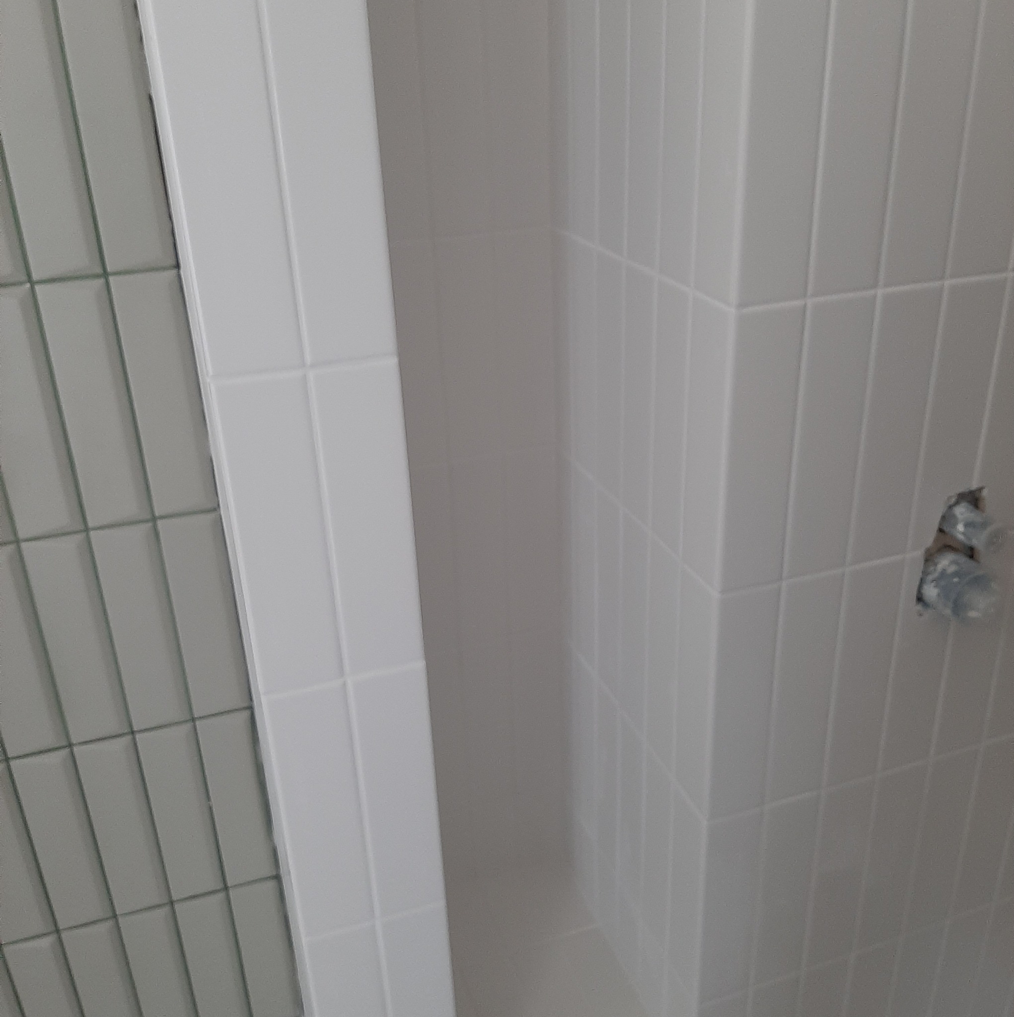 Wnęka prysznicowa wyłożona białymi, prostokątnymi płytkami, z widocznymi wystającymi rurami instalacji wodnej przed montażem armatury.