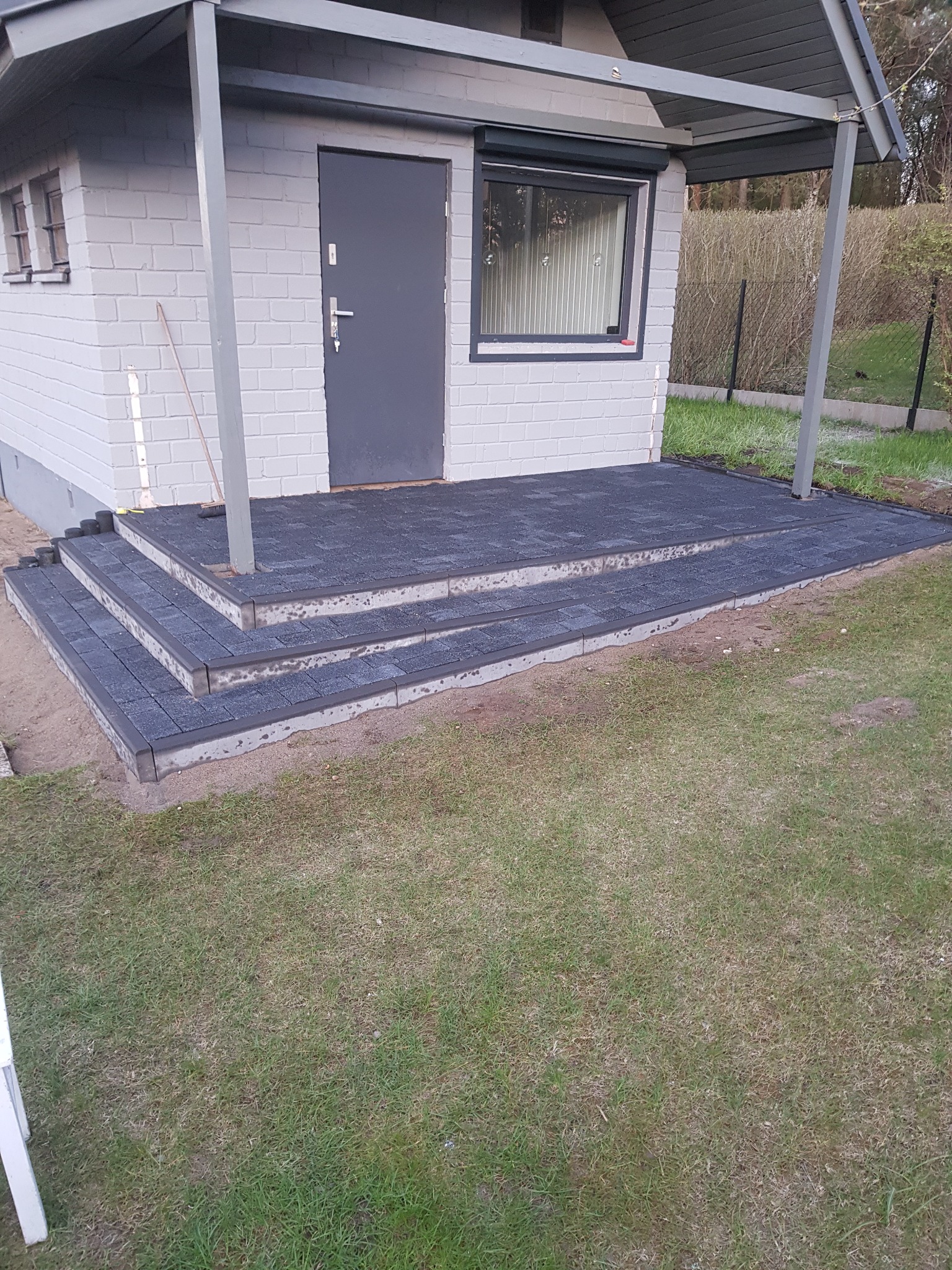 Nowo ułożone, ciemnoszare schody z kostki brukowej prowadzące do budynku z jasnej cegły, widok z poziomu trawnika.