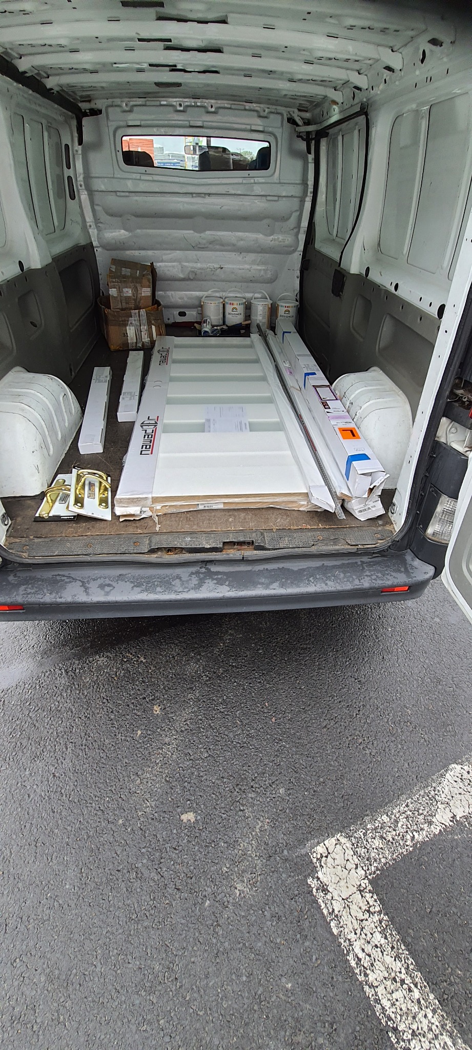 Wnętrze białego samochodu dostawczego z załadowanymi drzwiami wewnętrznymi w opakowaniach, puszkami farby i akcesoriami do montażu.