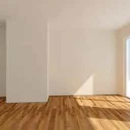 Puste, jasne pomieszczenie z drewnianą podłogą, białymi ścianami i dużym oknem balkonowym, przez które wpada naturalne światło.