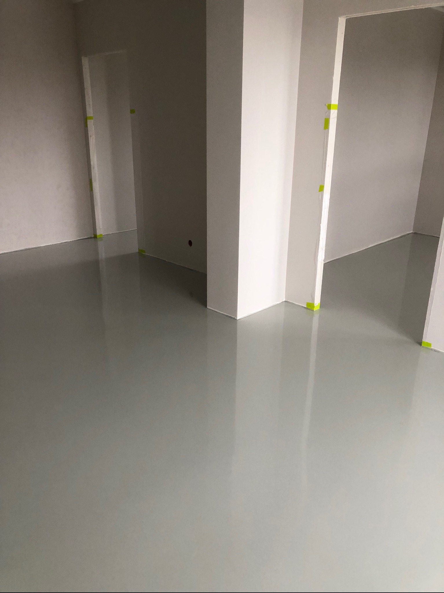 Jasnoszara, gładka posadzka w nowym wnętrzu z otworami drzwiowymi zabezpieczonymi żółtą taśmą malarską. Minimalistyczny design, świeżo wylana powierzchnia.