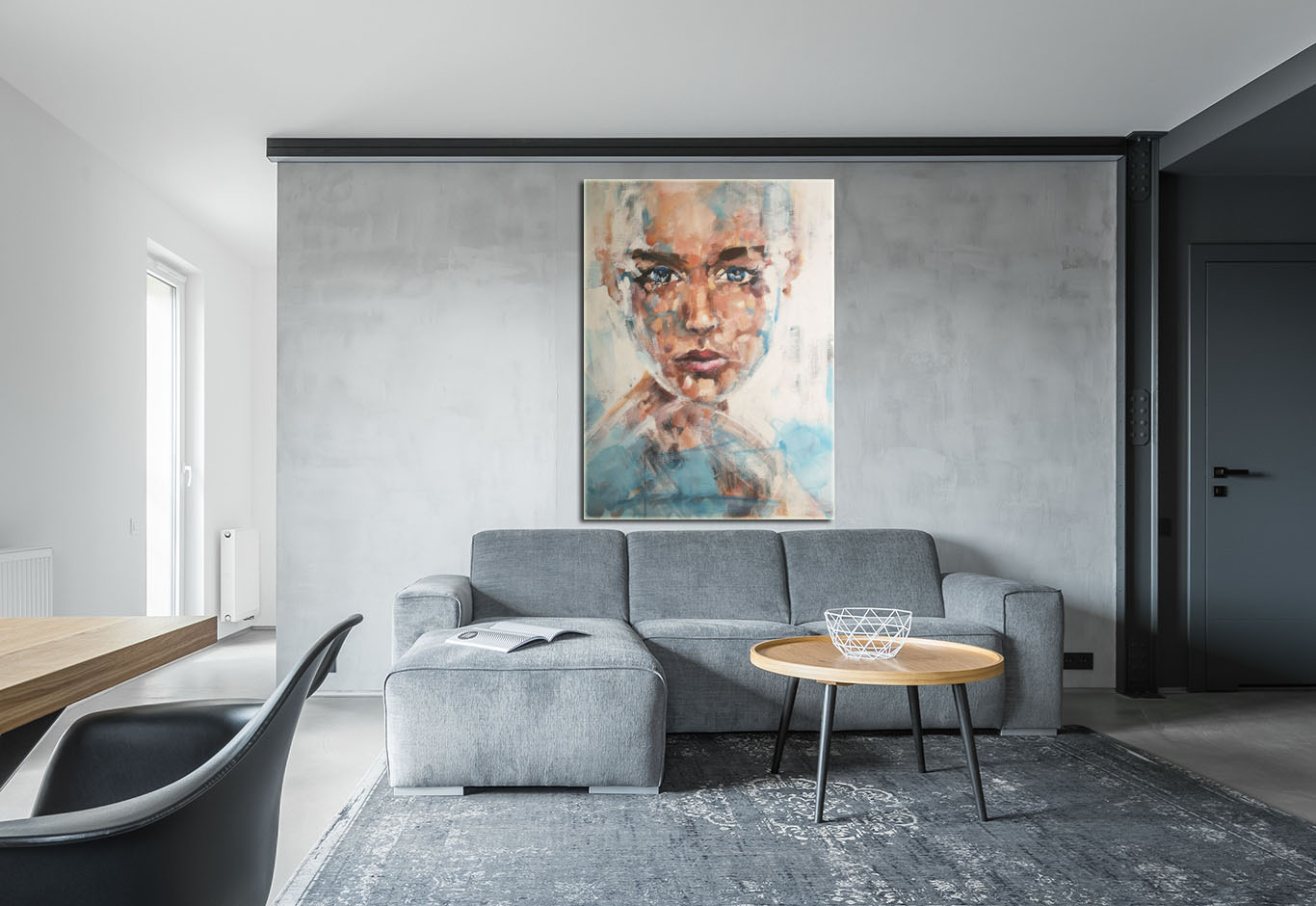 Szary salon z narożną sofą, okrągłym stolikiem kawowym i abstrakcyjnym portretem kobiety na ścianie z betonu architektonicznego.