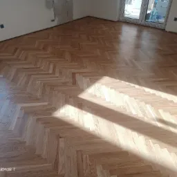 Ułożony parkiet w jodełkę z widocznym padającym światłem słonecznym, ściany przygotowane do malowania.