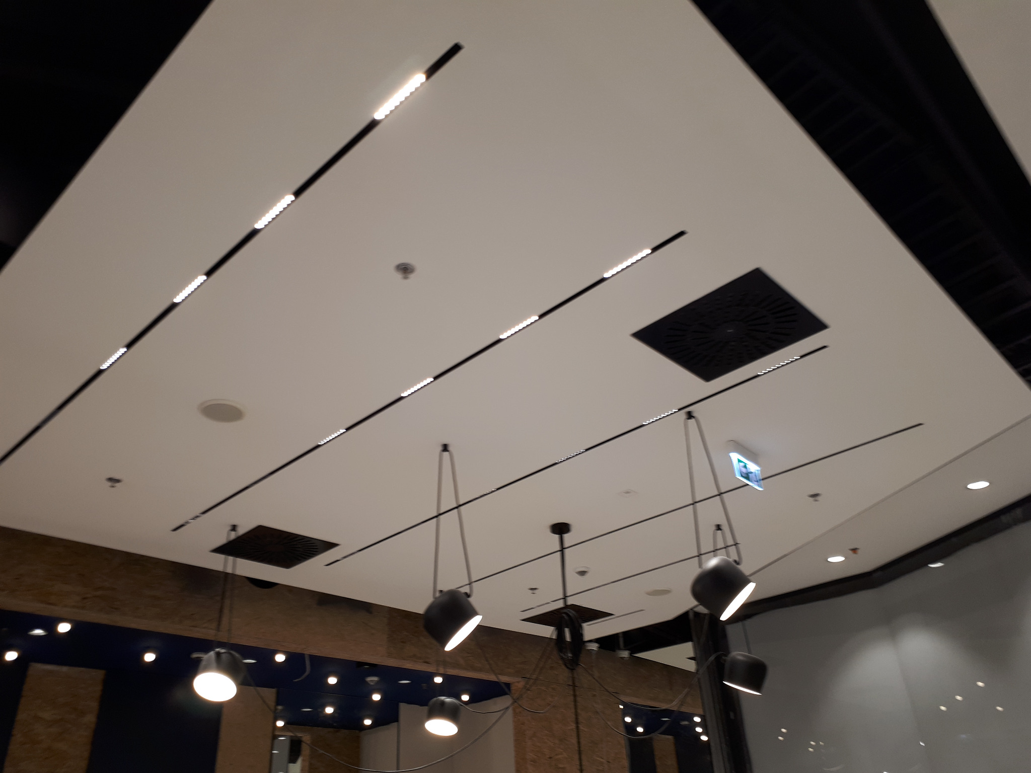 Sufit podwieszany z oświetleniem liniowym LED i czarnymi, wiszącymi lampami w nowoczesnym biurze lub lokalu usługowym.