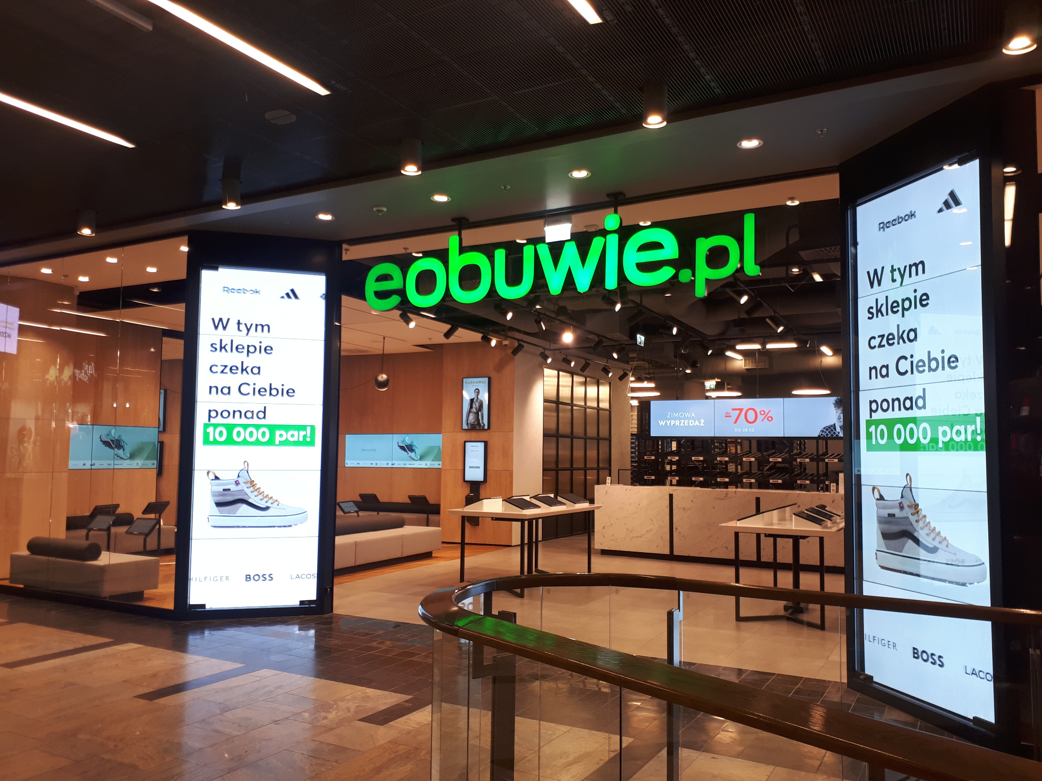 Nowoczesne wnętrze sklepu obuwniczego eobuwie.pl z jasnym oświetleniem, prezentujące ekspozycje butów na ekranach LED i minimalistyczne meble.