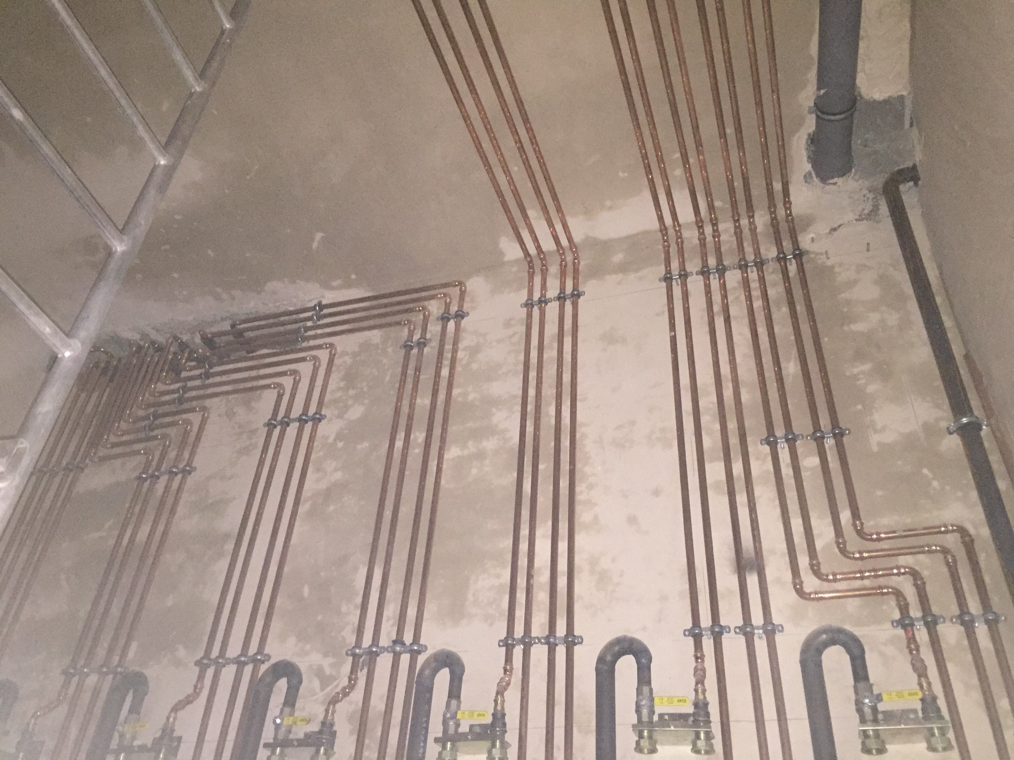 Miedziane rury centralnego ogrzewania zamontowane na ścianie w surowym stanie, z widocznymi zaworami i mocowaniami.