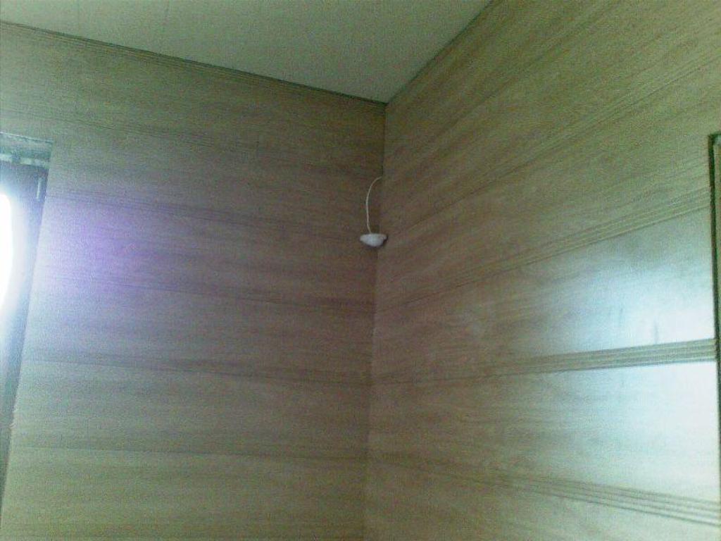 Sufit podwieszany i ściana wykończone panelami imitującymi drewno z widocznym fragmentem okna i lampą sufitową.