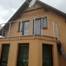 Pomarańczowy dom z balkonem zabezpieczonym nowoczesną balustradą ze stali nierdzewnej, drabina oparta o ścianę.