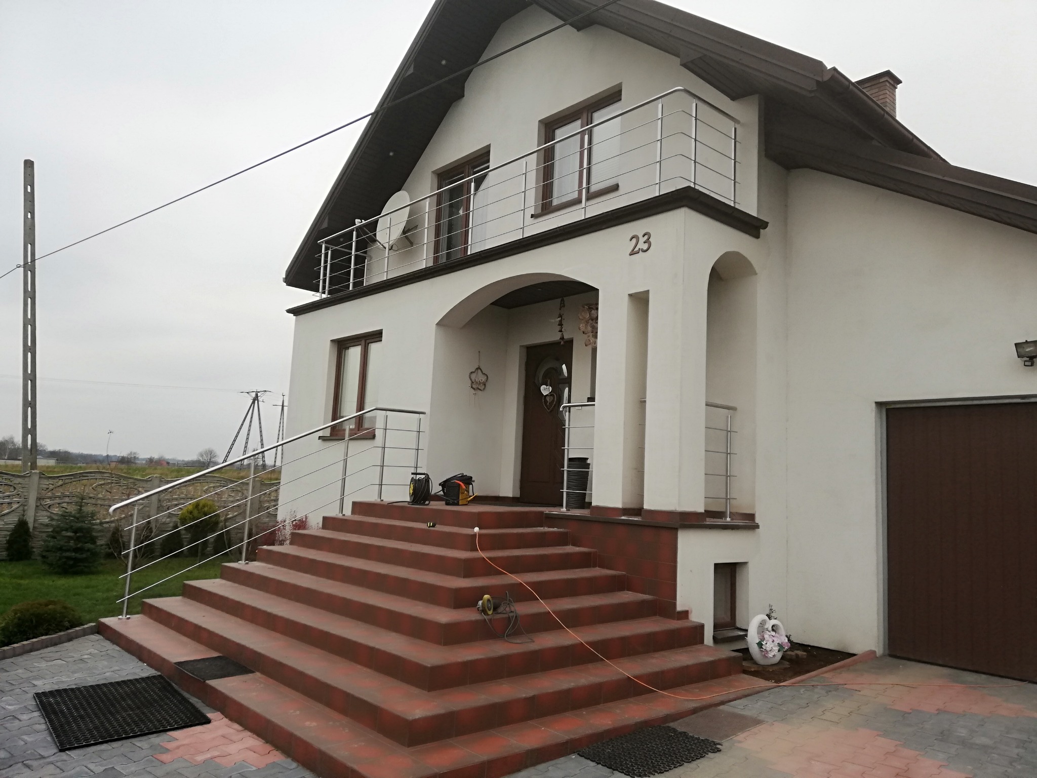 Dom jednorodzinny z nowymi, metalowymi balustradami na balkonie i przy schodach wejściowych, widoczne narzędzia sugerują trwający montaż.