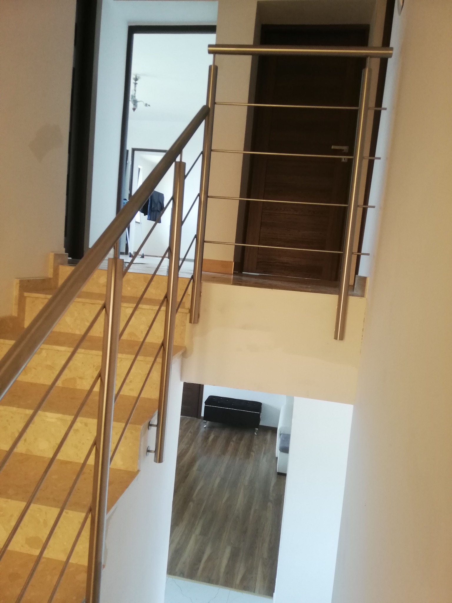 Schody z marmurowymi stopniami zabezpieczone metalową balustradą z poziomymi prętami, widok z góry na dół, w tle drzwi i fragment salonu.