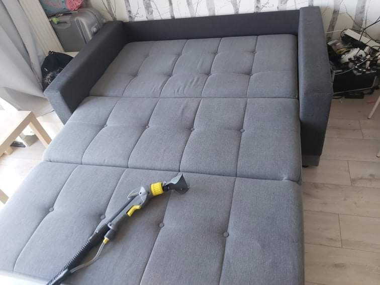 Szara rozkładana kanapa z tapicerką guzikową, czyszczona parowym odkurzaczem z żółtymi akcentami.