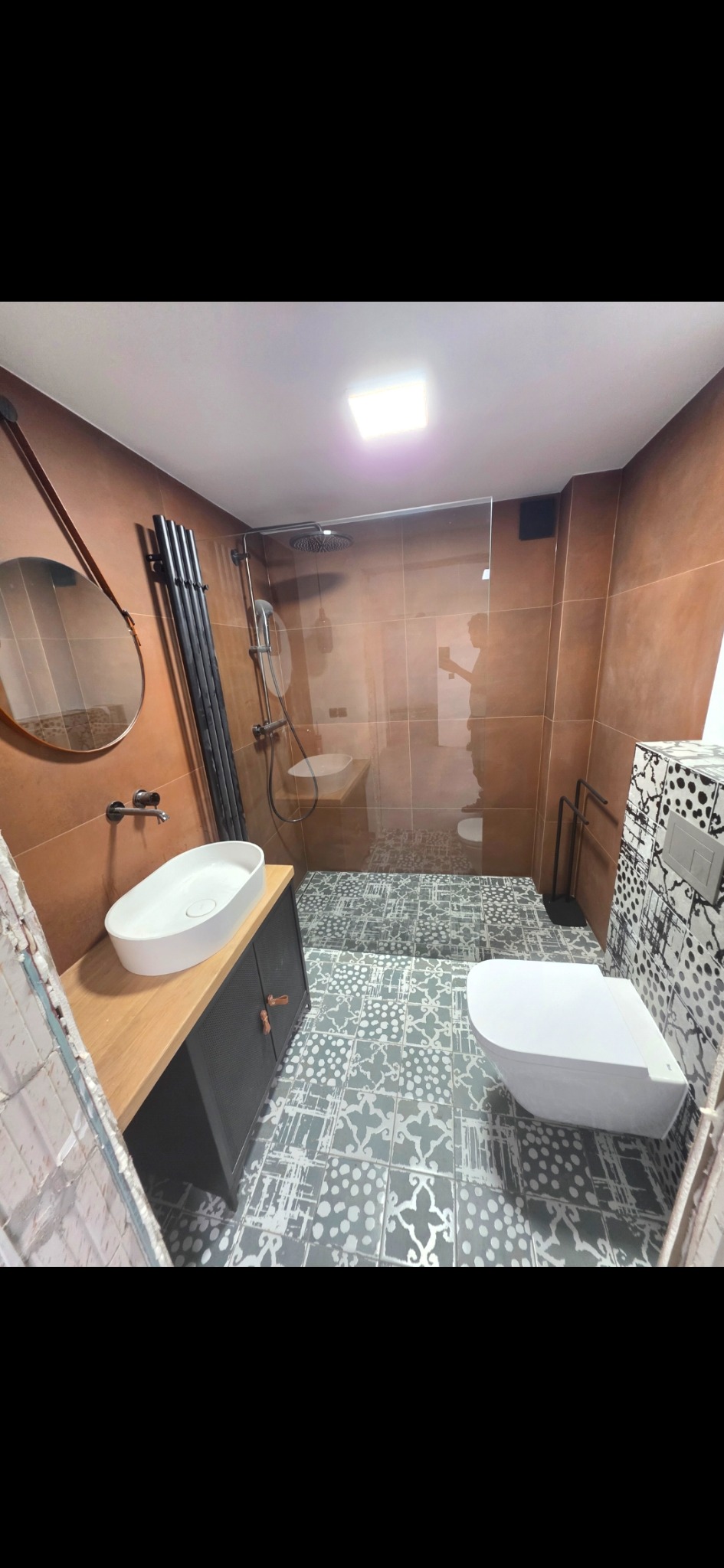 Wykończona łazienka z brązowymi płytkami, kabiną prysznicową, umywalką na szafce z drewnianym blatem i toaletą. Wzór płytek podłogowych w stylu vintage.