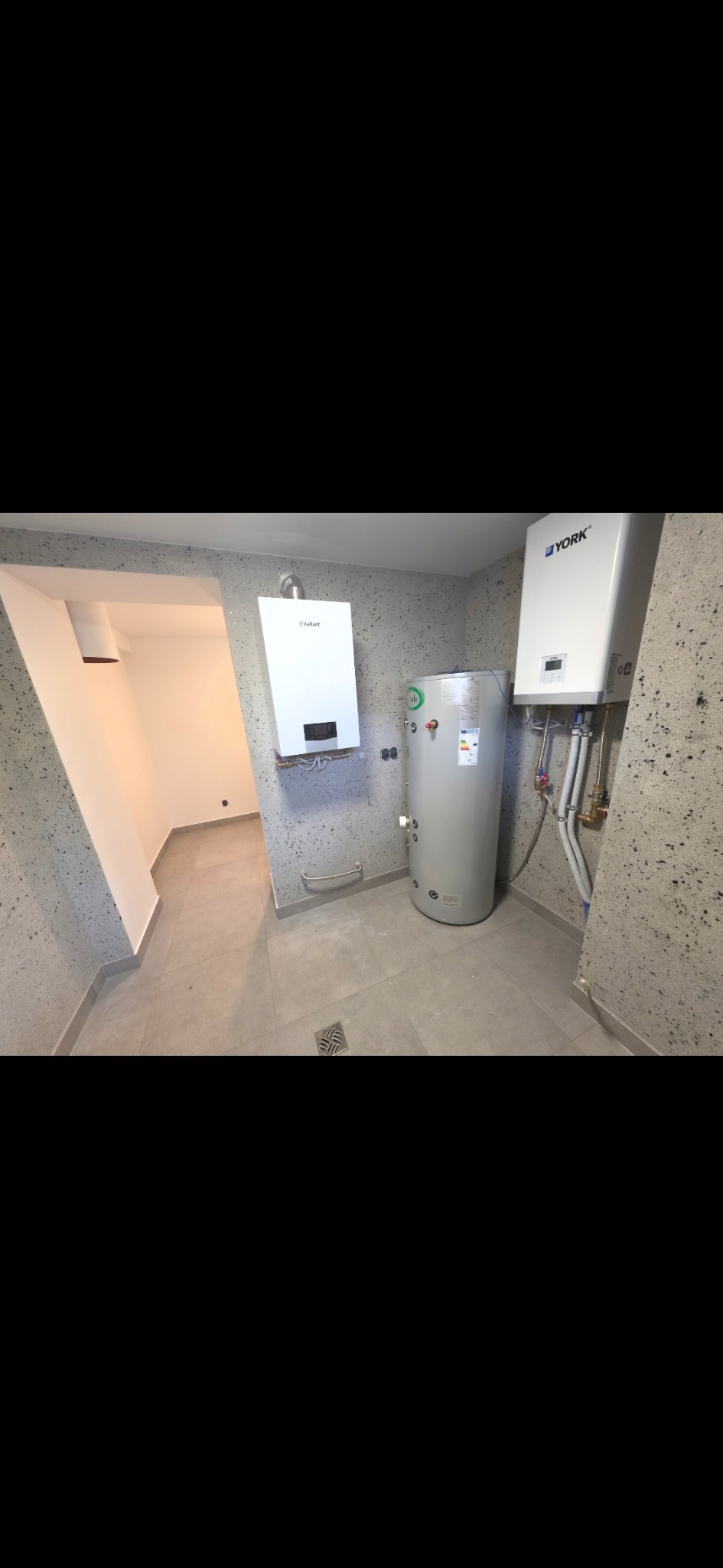 Kotłownia z dwoma piecami gazowymi (Vaillant i York) oraz zasobnikiem ciepłej wody. Ściany wykończone tynkiem strukturalnym, szare płytki podłogowe.