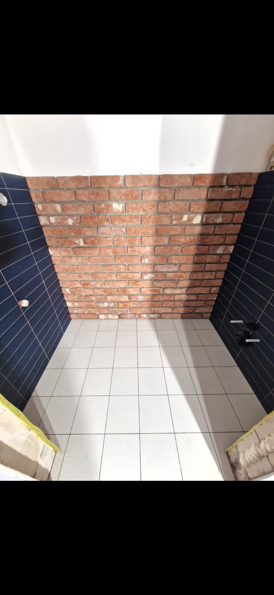 Wykończona łazienka z białą podłogą z płytek, ciemnoniebieskimi ścianami z płytek i ścianą z cegły. Widok z góry, ukończony remont.