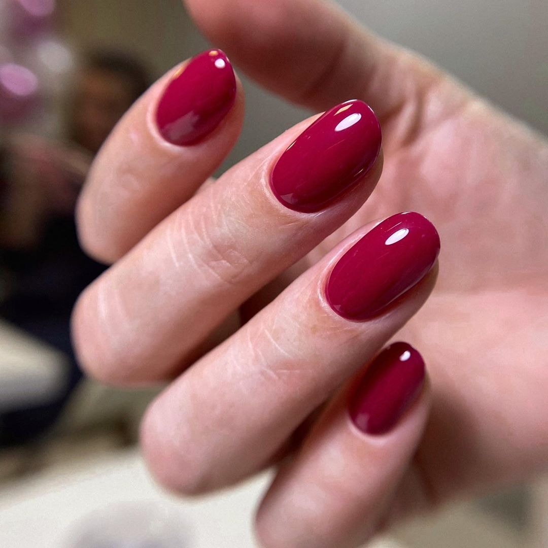 Dłoń z pomalowanymi na intensywny, ciemnoczerwony kolor paznokciami o owalnym kształcie, z widocznym połyskiem lakieru.