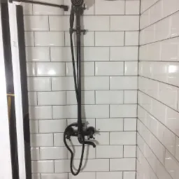 Nowoczesna kabina prysznicowa z czarną armaturą w stylu retro, białe kafelki ułożone w cegiełkę z ciemną fugą, widoczne niedokończone prace przy suficie.