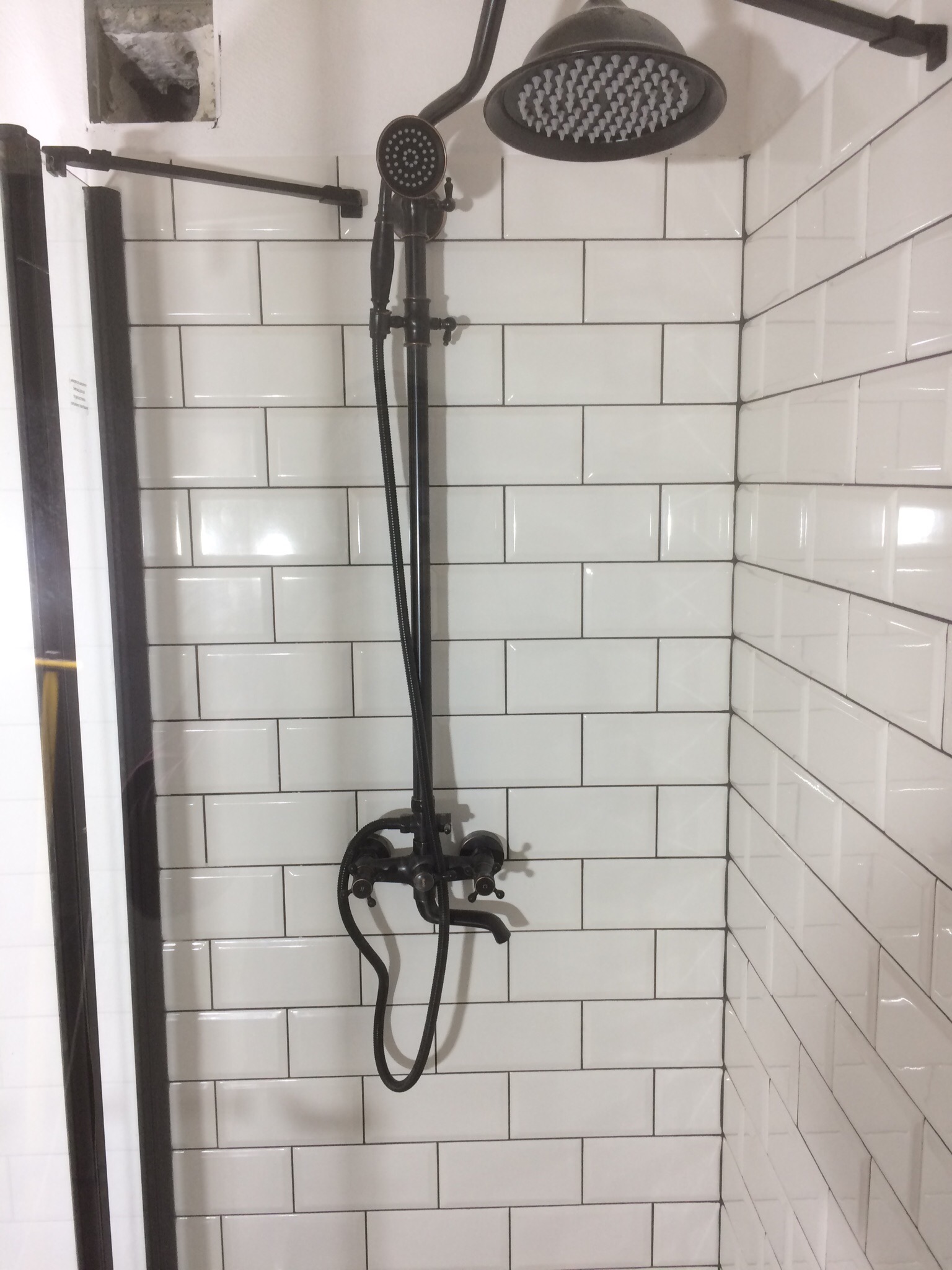 Nowoczesna kabina prysznicowa z czarną armaturą w stylu retro, białe kafelki ułożone w cegiełkę z ciemną fugą, widoczne niedokończone prace przy suficie.