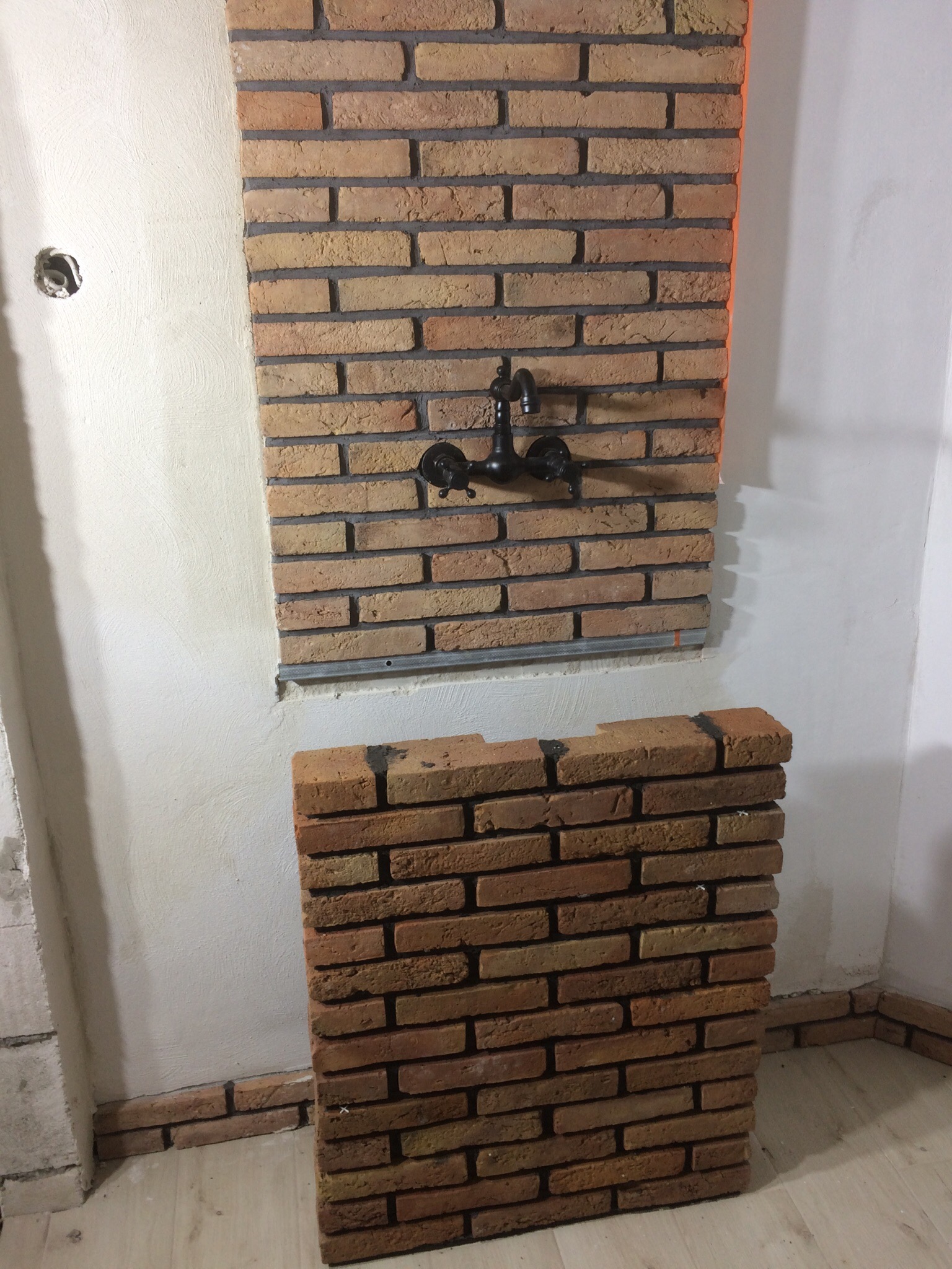 Montaż dekoracyjnej ściany z cegieł klinkierowych w łazience w Kraśniku, z widoczną armaturą i częściowo ułożonym fragmentem na podłodze.