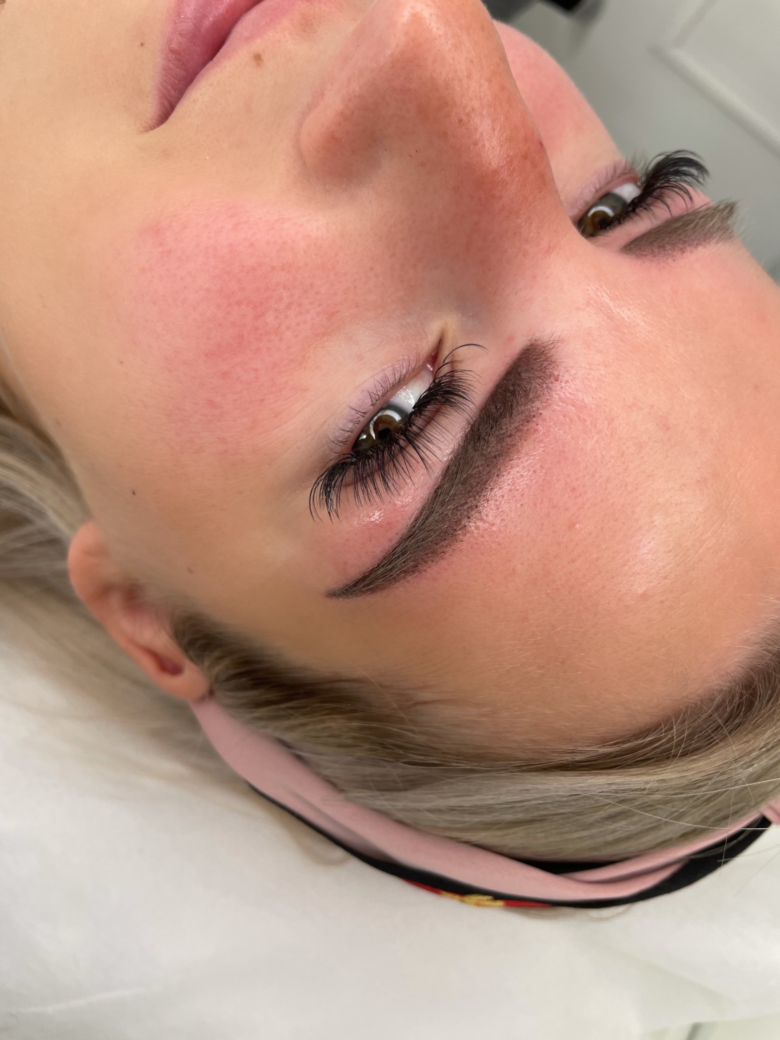 Zbliżenie na twarz kobiety po zabiegu przedłużania rzęs i stylizacji brwi, z widocznym zaczerwienieniem skóry wokół brwi i oczu.