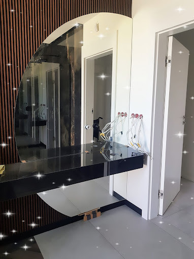 Owalne lustro łazienkowe z czarnym blatem, zamontowane na ścianie z drewnianymi panelami. Widoczne przewody elektryczne do oświetlenia.