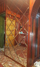 Ściana z lustrzanych rombów w drewnianej ramie, tworząca dekoracyjny wzór. Widoczne drewniane panele na ścianach i fragment podłogi z wzorzystym dywanem.