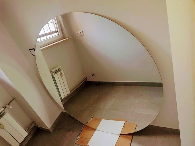 Okrągłe lustro bez ramy o dużej średnicy, opierające się o ścianę w jasnym pomieszczeniu ze skosami, widoczne kartony na podłodze.